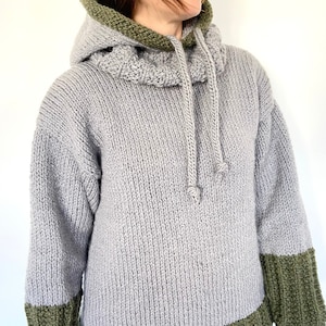 Op de afbeelding: Een grijze hoodie met groene bies aan de capuchon, manchetten en zoom. De trui heeft een capuchon met trekkoord en een losse pasvorm.