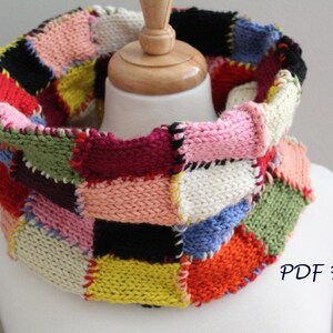 May include: A colorful knitted cowl with a patchwork design. The cowl is made up of squares of different colors, including red, pink, yellow, green, blue, and white. The cowl is shown on a white mannequin. The text "PDF Pattern" is visible in the lower right corner of the image.