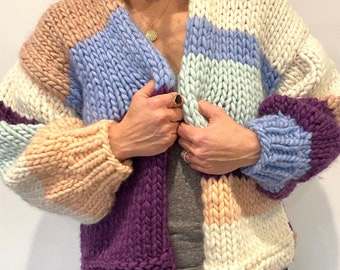 May include: A chunky knit cardigan with a striped pattern in shades of purple, pink, blue, and white. The cardigan has a relaxed fit and a v-neck.