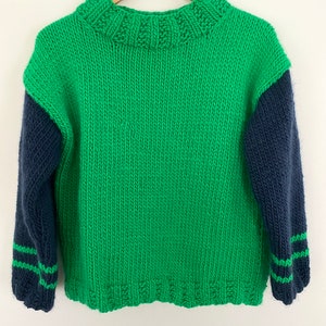 May include: A green and navy blue knitted sweater with a crew neck and long sleeves. The sleeves are a contrasting navy blue color with green stripes at the cuffs.