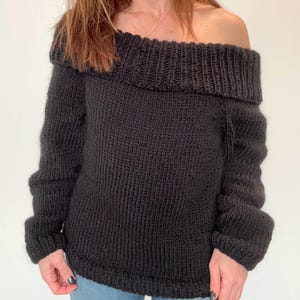 May include: A black off-the-shoulder knitted sweater with long sleeves.