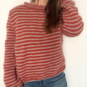 May include: A red and beige striped sweater with a crew neck. The sweater has long sleeves and is made of a thick, knitted material. The stripes are horizontal and evenly spaced, creating a classic, cozy look.