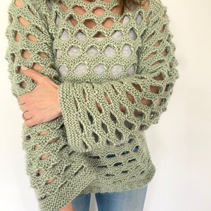 Peut inclure: Un pull en tricot vert sauge avec un grand motif ajouré sur toute la surface. Le pull est ample et à manches longues.