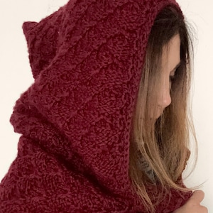 Könnte beinhalten: Burgunderfarbener Kapuzenschal mit einem strukturierten Strickmuster. Die Kapuze ist so konzipiert, dass sie Kopf und Hals bedeckt und Wärme und Stil bietet. Der Schal besteht aus einem weichen, dicken Material.