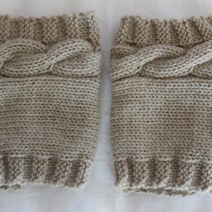 May include: A pair of beige knitted leg warmers with a cable knit design.