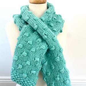 May include: A teal blue knitted scarf with a textured bobble stitch pattern.
