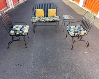 May include: Outdoor patio furniture set with a black metal frame. The set includes a loveseat, two swivel chairs, and a small side table. Cushions feature a floral pattern, and the pillows are yellow.
