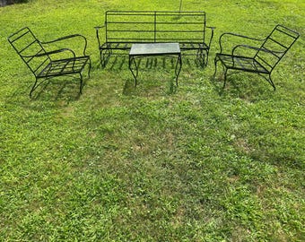 May include: A black metal outdoor furniture set on a grassy lawn. The set includes two armchairs, a loveseat, and a small rectangular table. The furniture has a simple, wrought-iron design.
