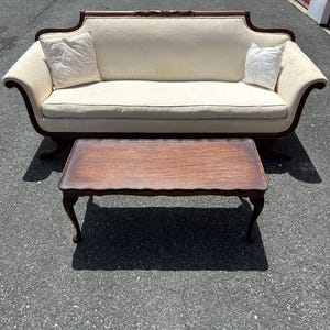 May include: A white upholstered sofa with carved wooden arms and legs, paired with a dark wood coffee table with a carved edge and four legs.