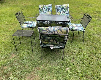 May include: Outdoor patio furniture set with a black metal frame. The set includes a rectangular table, four chairs, and a small side table. The chair cushions feature a tropical leaf pattern in shades of green and blue.