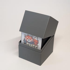 Könnte beinhalten: Eine graue Kartenspielbox mit einer Illustration eines Roten Pandas auf der Vorderseite. Die Box ist geöffnet und die Karten sind im Inneren sichtbar.