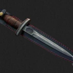 Peut inclure: Un poignard argenté avec une poignée en cuivre torsadée est inséré dans un fourreau en cuir noir avec des coutures rouges. Le poignard a une pointe pointue et une lame légèrement incurvée.