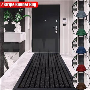 May include: A black and grey striped doormat with 7 stripes. The doormat is placed in front of a black door in a hallway. The doormat is a runner style and is long enough to cover the entire width of the doorway. The doormat is made of a durable material and is designed to withstand heavy foot traffic.