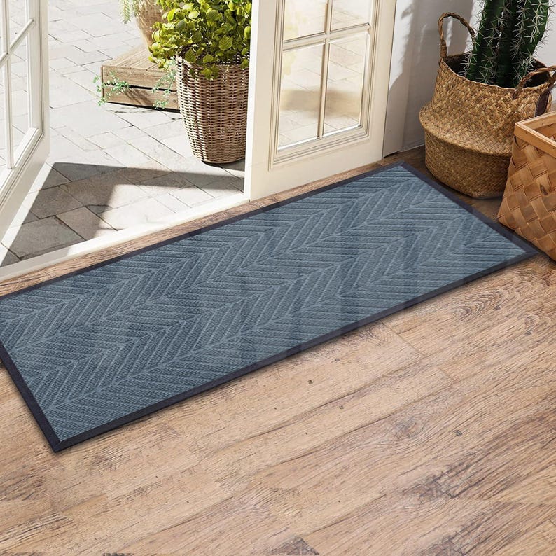 May include: A gray doormat with a herringbone pattern. The doormat is placed in front of a wooden door with a glass panel.