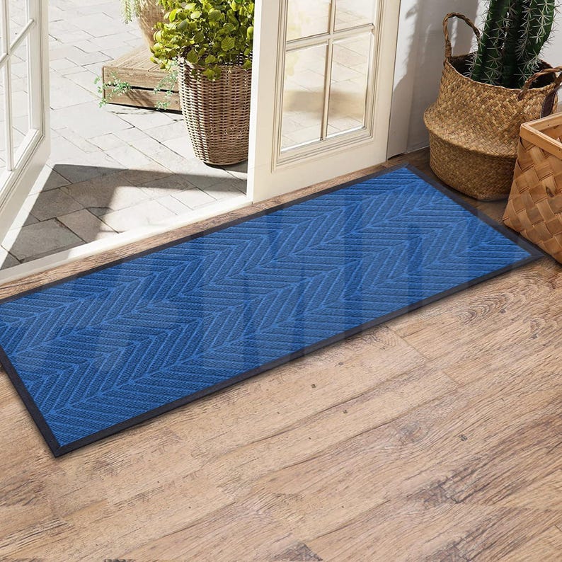 May include: A blue doormat with a herringbone pattern. The doormat has a black border and is placed on a wooden floor.