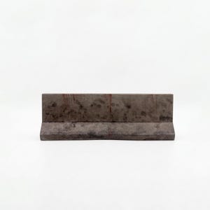 K&ouml;nnte beinhalten: Rechteckige Betonbarriere in Dunkelgrau mit verwittertem Aussehen. Sie hat eine flache Oberseite und eine leicht abgewinkelte Basis. Die Oberfl&auml;che weist subtile Textur- und Farbvariationen auf, geeignet f&uuml;r verschiedene Anwendungen.