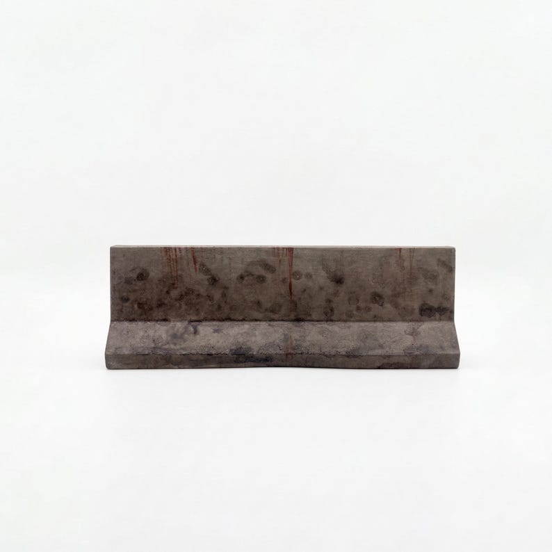 K&ouml;nnte beinhalten: Rechteckige Betonbarriere in Dunkelgrau mit verwittertem Aussehen. Sie hat eine flache Oberseite und eine leicht abgewinkelte Basis. Die Oberfl&auml;che weist subtile Textur- und Farbvariationen auf, geeignet f&uuml;r verschiedene Anwendungen.