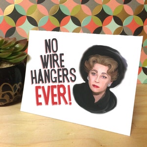 May include: A white card with the text "NO WIRE HANGERS EVER!" in red and black lettering. A woman with dark hair and a black hat is pictured on the card.