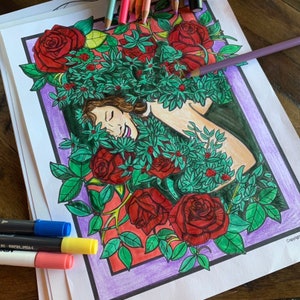 May include: A partially coloured illustration of a woman's face and upper body, nestled amongst red roses and green leaves. The artwork is framed in a purple border. Colouring pencils and markers are visible.