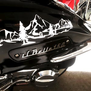 May include: A black motorcycle with a white mountain and tree decal on the back fender. The motorcycle has a chrome rear fender and a chrome exhaust pipe. The motorcycle has a silver emblem that says "Bella 150".