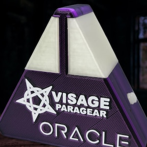 May include: A purple, triangular object with the text "VISAGE PARAGEAR ORACLE" in white. The object has a white, triangular top and a purple, textured base. A white star-like symbol is on the left side.