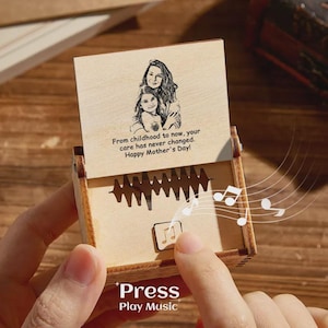 May include: A wooden music box featuring an engraved image of a mother and child. The lid displays the text "From childhood to now, your care has never changed. Happy Mother's Day!" and "Press Play Music". Musical notes are shown.