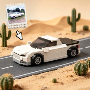 Op de afbeelding: Een witte en zwarte speelgoedauto gemaakt van plastic bouwstenen, met een zwart dak en getinte ramen, staat op een miniatuurweg. De scène omvat speelgoedcactussen en zandduinen, met een kleine afbeelding van een auto op een witte tablet.
