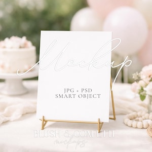 May include: A white sign on a gold stand with the word "Mockup" in a script font. The sign is surrounded by a cake, flowers, and balloons, suggesting a celebration or event. Text on the sign reads "JPG + PSD SMART OBJECT".