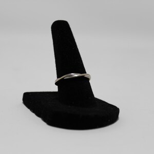 May include: A silver ring with a twisted design is displayed on a black ring holder. The ring has a smooth, polished finish and a simple, elegant style. The ring is a piece of jewellery.