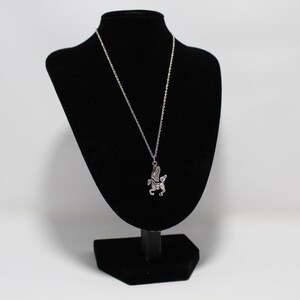 May include: A silver necklace with a winged horse pendant on a black velvet display stand.