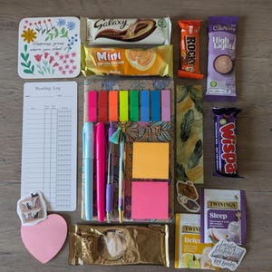 May include: A flat lay of various items including a reading log, chocolate bars, sticky notes, pens, tea bags, and a heart-shaped sticky note with the text "Easily Distracted by Books".