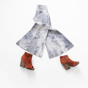 Può includere: Un paio di pantaloni a gamba larga con stampa pitonata grigia e bianca, abbinati a due stivaletti in camoscio color ruggine. Gli stivaletti presentano punte aperte, cerniere laterali e tacchi a blocco in legno scuro e spesso.