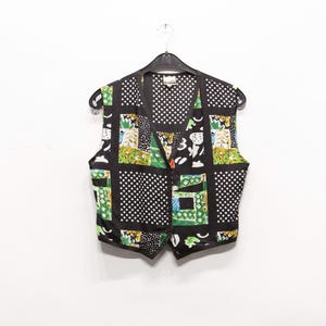 Puede incluir: Un chaleco vintage con diseño de patchwork. El chaleco presenta un fondo negro con lunares blancos y patrones cuadrados coloridos. Tiene cuello en V, cierre de botones y está colgado de una percha negra.