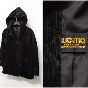 Könnte beinhalten: Schwarze Cord-Kapuzenjacke mit Knebelverschlüssen. Die Jacke hängt an einem Kleiderbügel vor weißem Hintergrund. Die Jacke hat ein Etikett innen mit der Aufschrift "suoma" und "Made in Finland".