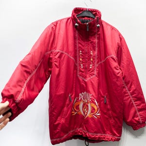 Puede incluir: Chaqueta roja vintage con cuello alto y cierre de cremallera. La chaqueta presenta detalles de costura blancos y un diseño bordado en el pecho con la palabra "PROINE". Tiene dos bolsillos con cremallera y un cordón en la parte inferior.