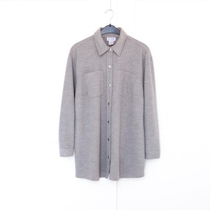 Pode incluir: Uma camisa de manga comprida com botões em cinza discreto, pendurada em um cabide preto. A camisa apresenta dois bolsos no peito e uma gola clássica. O tecido parece ser um material macio e tecido.