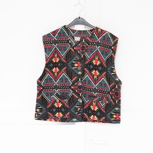 Peut inclure: Un gilet sans manches avec une base gris anthracite orné d'un motif géométrique aux tons rouge, jaune et bleu sarcelle. Le vêtement présente une encolure en V, une fermeture boutonnée à l'avant avec trois boutons et deux petites poches.