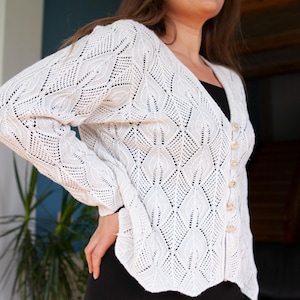 May include: A white crocheted cardigan with a button-up front. The cardigan has a delicate, open-weave pattern.
