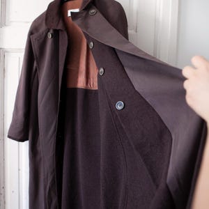 May include: A long brown coat with a brown corduroy collar and a brown lining. The coat has a button closure and is open to reveal the lining.