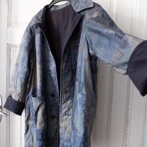 Könnte beinhalten: Eine lange, blau-graue gemusterte Jacke mit schwarzem Futter und Knopfleiste. Die Jacke hat einen Kragen und lange Ärmel mit schwarzen Bündchen.