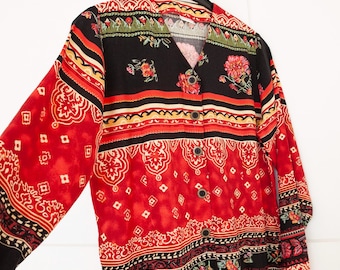May include: A red, black, and cream button-up shirt with a paisley pattern and floral accents. The shirt has a V-neck and long sleeves.