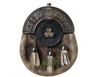 May include: A brown and white fur sporran with a silver and black metal embellishment featuring a Celtic knot design and a shamrock. The sporran has three tassels.