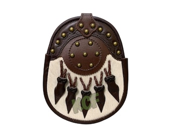 Puede incluir: Una sporran de cuero marrón con un panel de piel blanca y borlas decorativas. La sporran presenta una parte superior circular de cuero marrón con tachuelas de latón y un cierre de solapa. Un accesorio escocés tradicional.