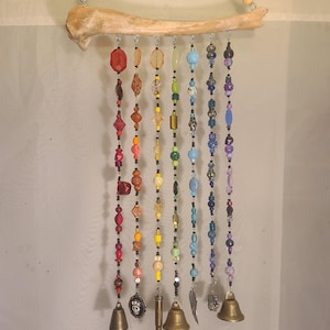 May include: A colorful wind chime with a natural bone top and hanging strands of beads in a rainbow of colors. The strands end with small brass bells, charms, and a bullet casing. The beads are various shapes and sizes.