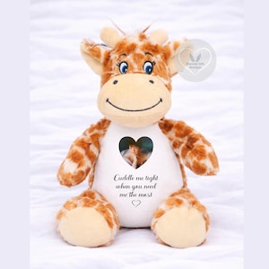 May include: A plush giraffe toy with brown and tan spots, featuring a white belly panel. The panel displays a heart-shaped photograph of a person and the printed text: Cuddle me tight when you need me the most, followed by a small heart icon.