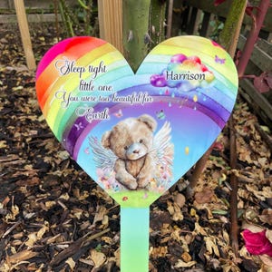 Könnte beinhalten: Ein herzförmiger Gartenstecker mit Regenbogenmuster und einer Teddybär-Illustration. Der Stecker trägt den Text "Sleep tight little one. You were too beautiful for Earth." und den Namen "Harrison".
