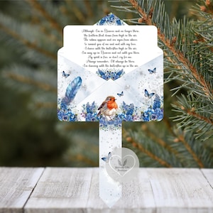 May include: A white memorial garden stake with a poem about a loved one in Heaven. The stake features a robin, blue flowers, butterflies, and a blue feather design. The text reads "Heavenly Gifts Boutique."