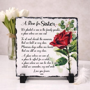 Pode incluir: Placa quadrada de ardósia com uma ilustração de rosa vermelha e o texto "A Rose for Sister". O poema inclui frases como "apreciar as memórias" e "Love you forever". A placa é suportada por um suporte preto.