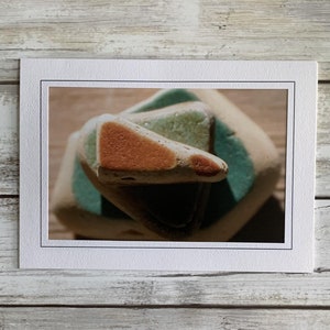 May include: A close-up of a stack of three ceramic tiles. The top tile is a triangular shape with a brown and green glaze. The middle tile is a square shape with a green glaze. The bottom tile is a rectangular shape with a brown glaze.