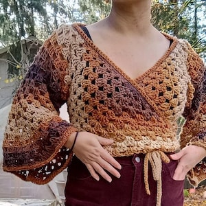 May include: A crochet wrap top in brown, tan, and purple hues. The top has a V-neck, long bell sleeves, and a tie waist. The openwork design gives a delicate look to this bohemian style garment. The garment is handmade.
